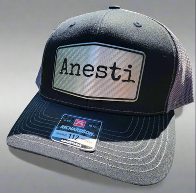 Black and gray cap with 'Anesti' logo on a wooden surface outdoors