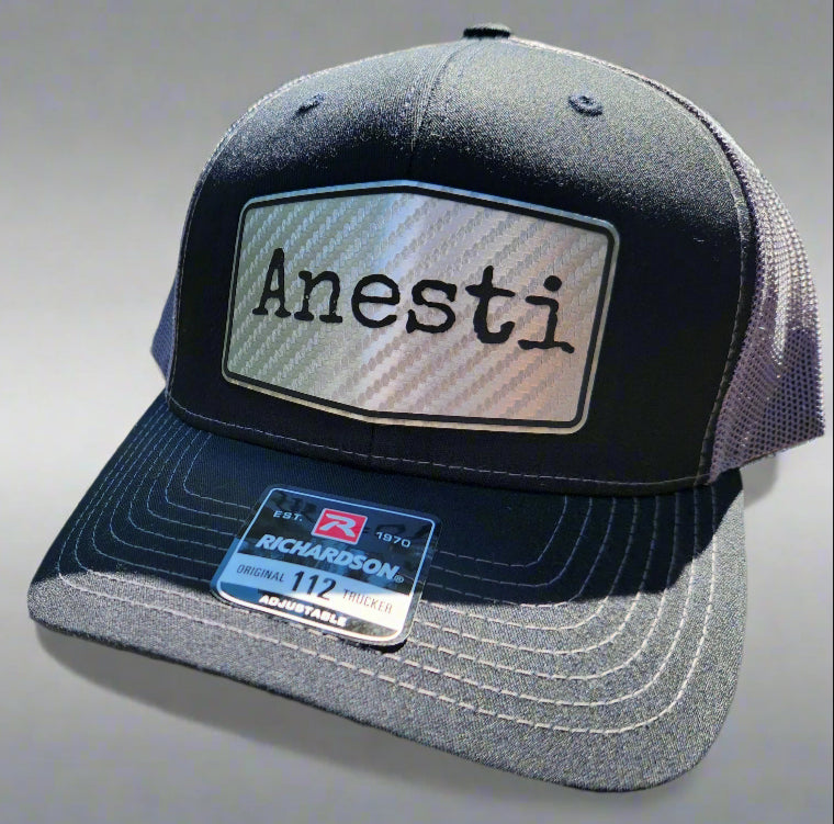 Black and gray cap with 'Anesti' logo on a wooden surface outdoors