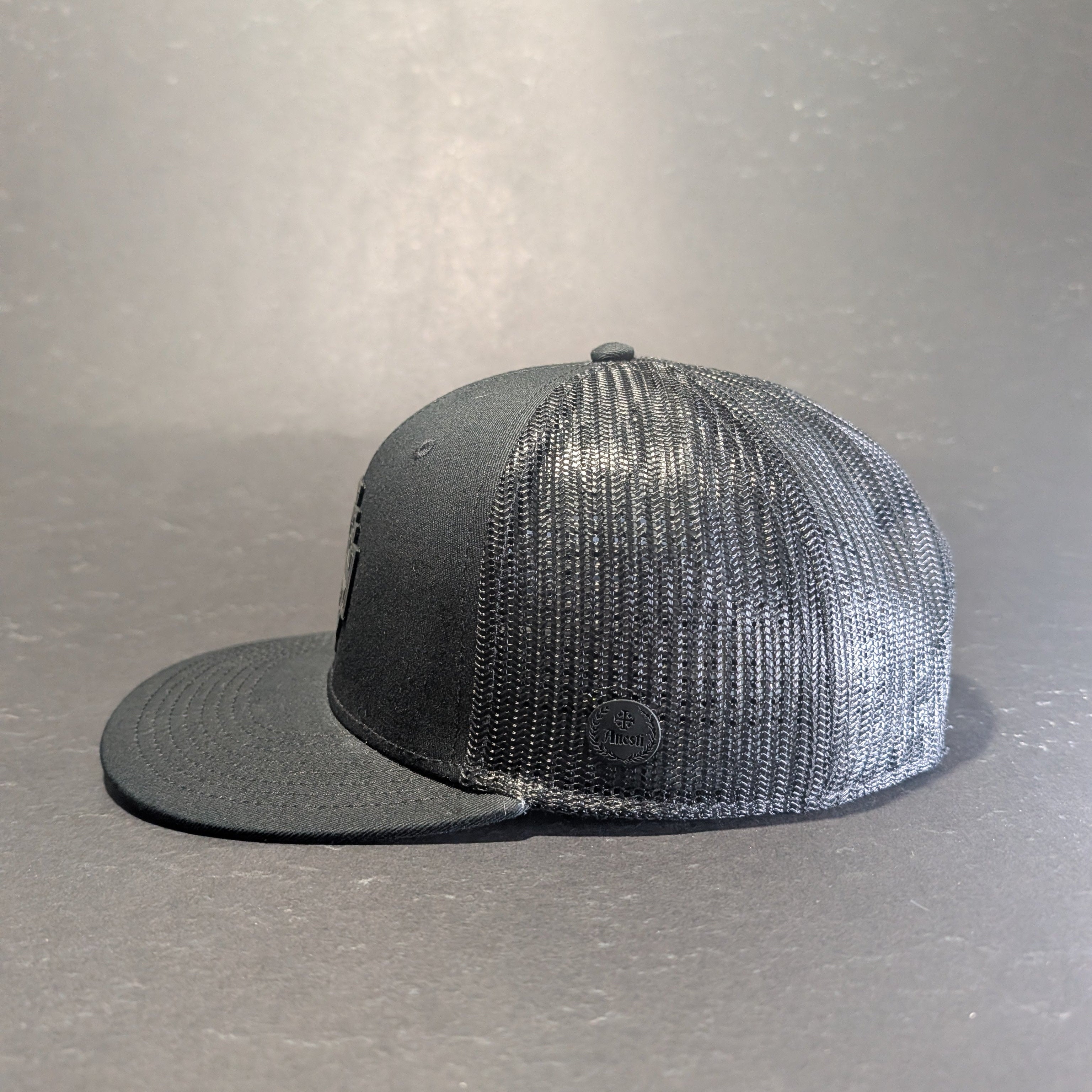 Jerusalem Cross Blackout all black flat bill snapback, side profile showing black mesh and Anesti leatherette crest